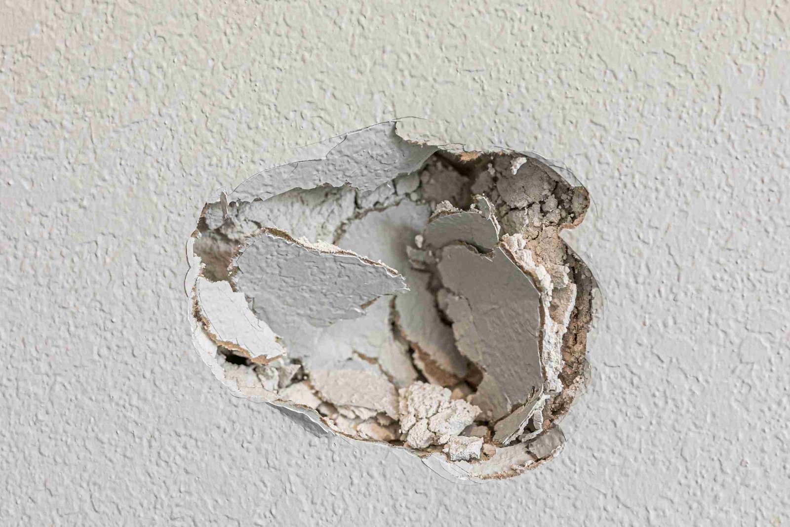 A hole in the wall of a hallways caused by a fist punching through the wall to create a large hole that needs repair.