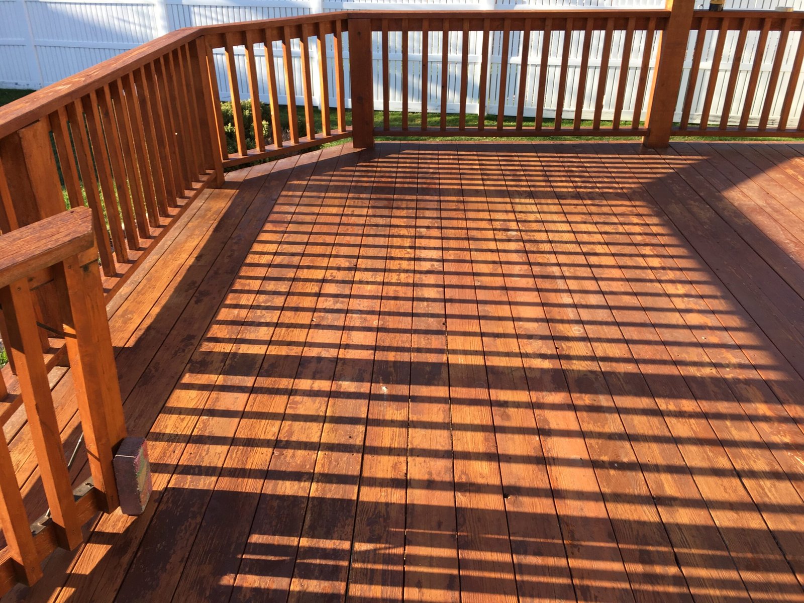 Freshly stained wooden backyard deck completed by Paint EZ, featuring a rich brown finish, clean railings, and sunlight casting striped shadows across the deck boards.