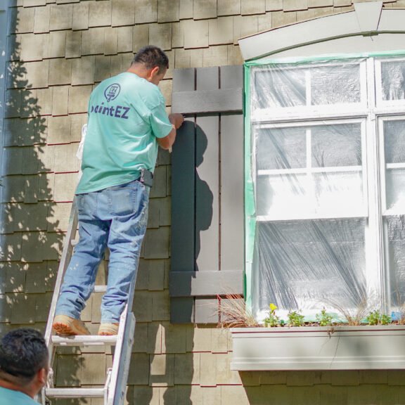 Paint EZ painter prepping a home exterior of for painting by taping down surface protection.