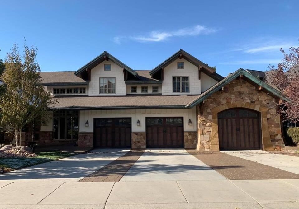 Three professionally painted dark wood-look garage doors on a stone and stucco home.