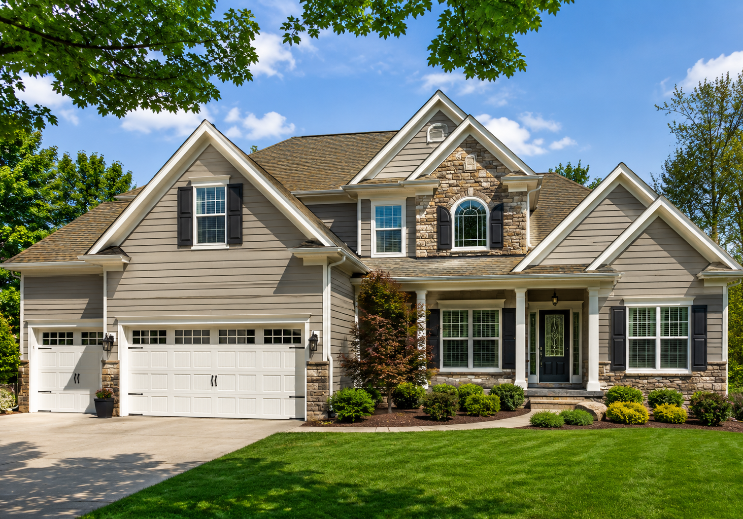 Two-story Chesterfield, MO home with taupe siding, stone accents, black shutters, white garage doors, and professionally maintained landscaping.