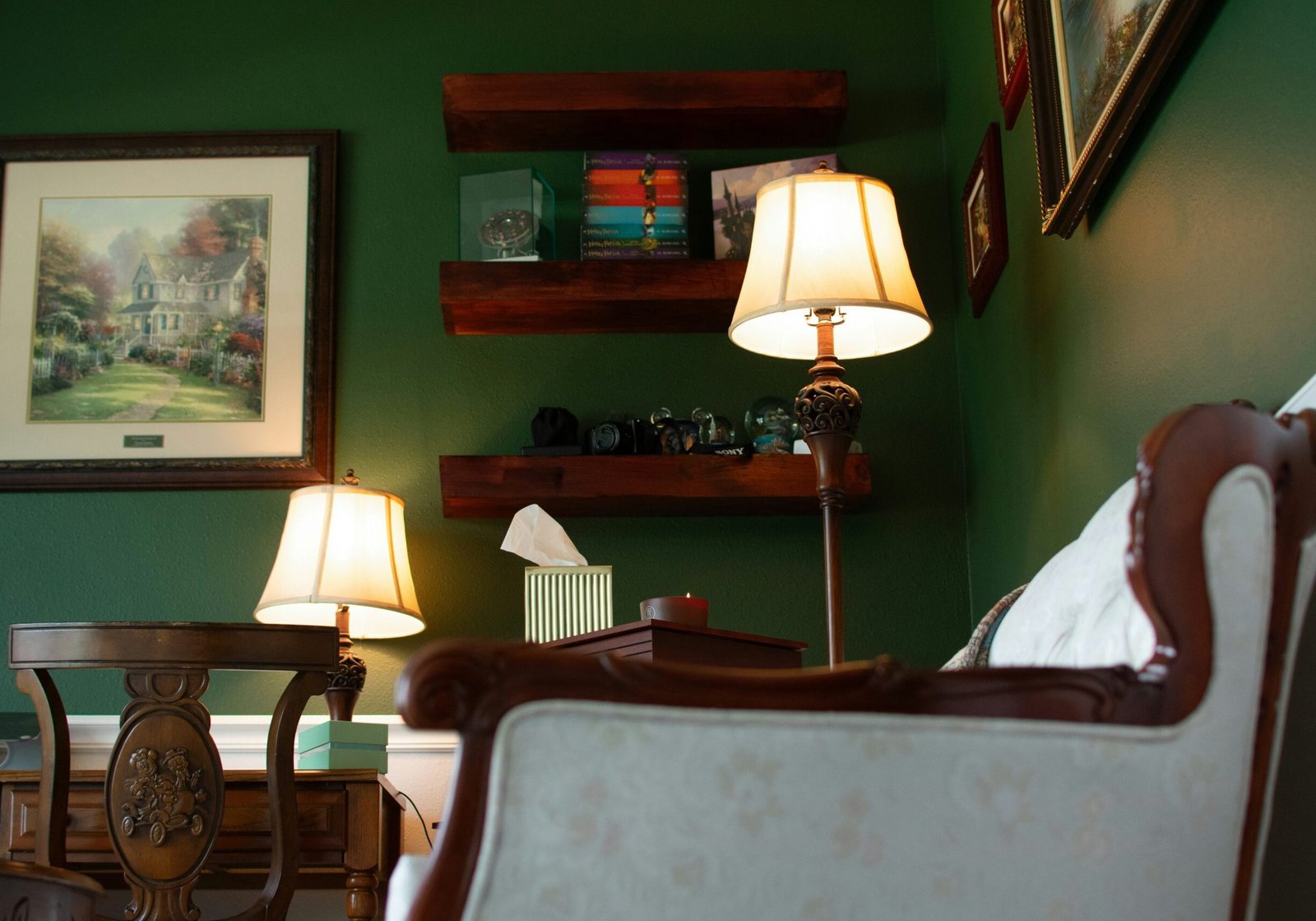 Living room with dark green painted walls, warm lighting, wood shelving, and traditional furniture