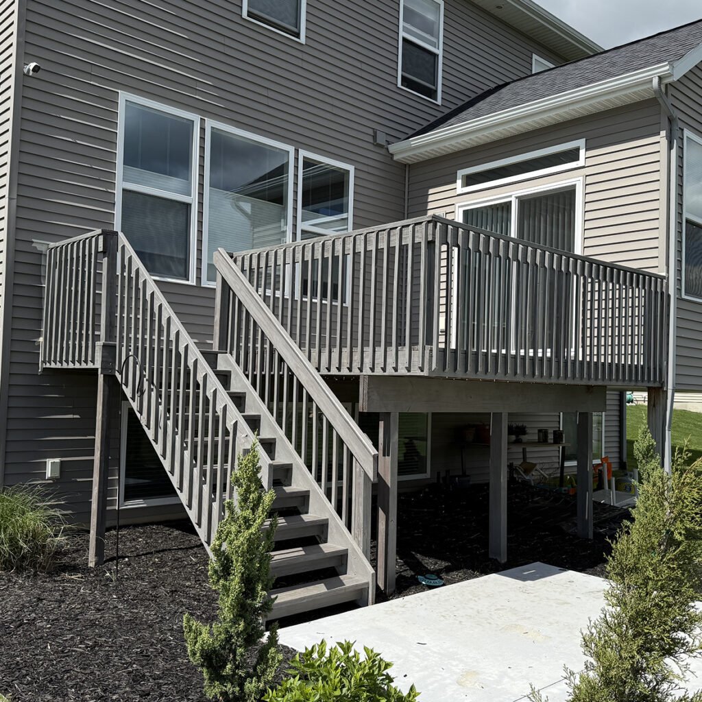 Freshly refinished gray backyard deck completed by Paint EZ, featuring updated railings, wide stairs, and a clean modern finish attached to a two-story home.
