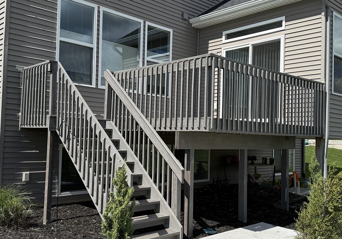 Freshly refinished gray backyard deck completed by Paint EZ, featuring updated railings, wide stairs, and a clean modern finish attached to a two-story home.