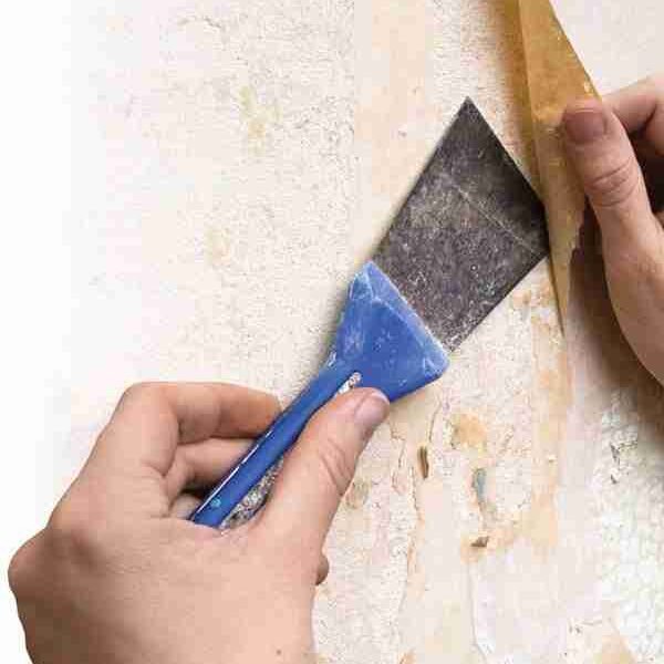 Paint EZ professional removing old wallpaper with scraper during wall preparation.