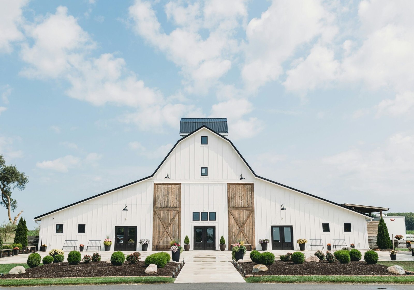 Large white barn converted into an event venue with landscaped entrance and modern design
