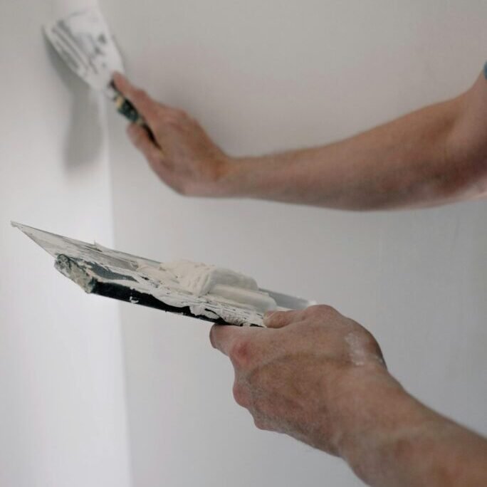 Drywall repair professional applying joint compound to patch and smooth an interior wall.