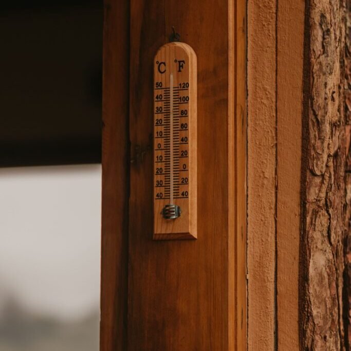 Outdoor thermometer mounted on a wooden wall for checking exterior painting temperatures.