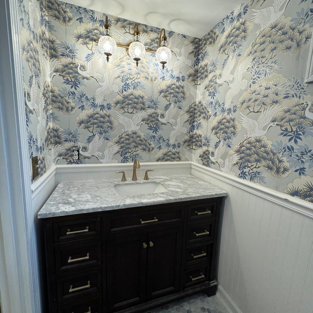 Blue and white crane-pattern wallpaper installed by Paint EZ in elegant powder bathroom with marble vanity.